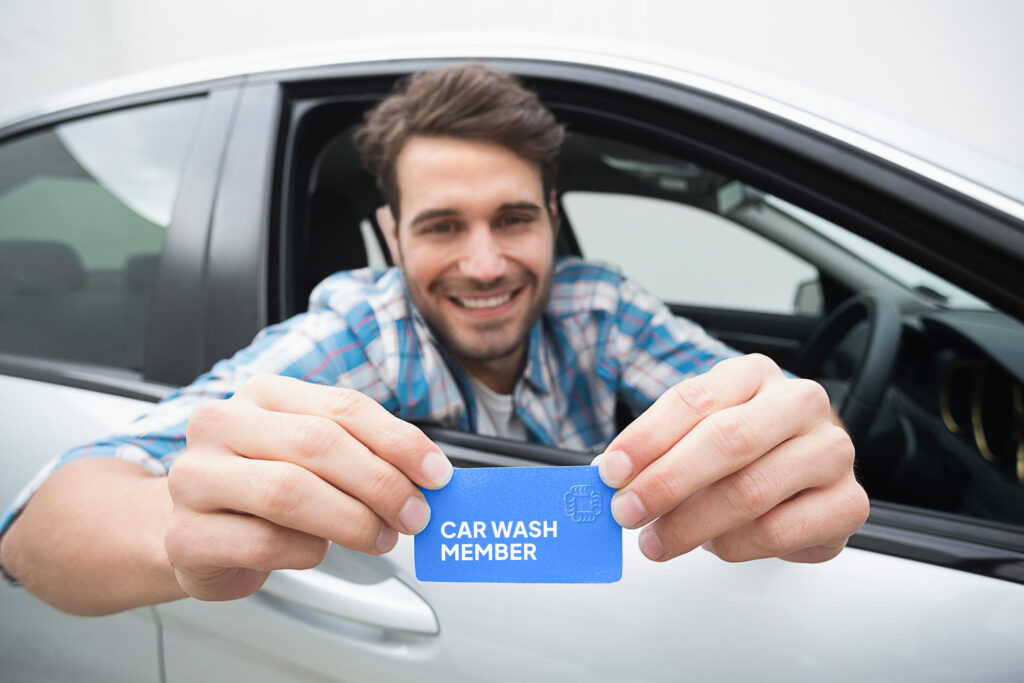 A man hanging out a car window while smiling and showing his car wash membership card